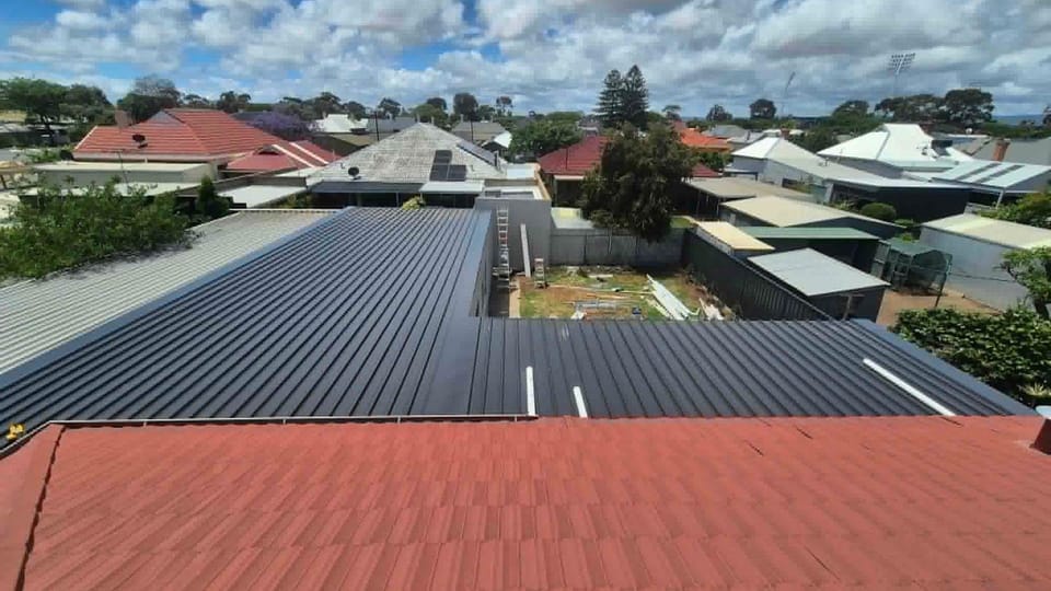 A new dark Colorbond roof by A1 Roofing over an Adelaide home, with neighbouring tiled roofs and a blue sky