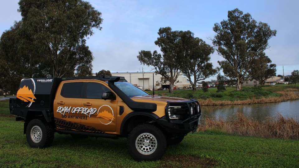 Roam Offroad's wrapped demo ute parked on the grass beside a lake