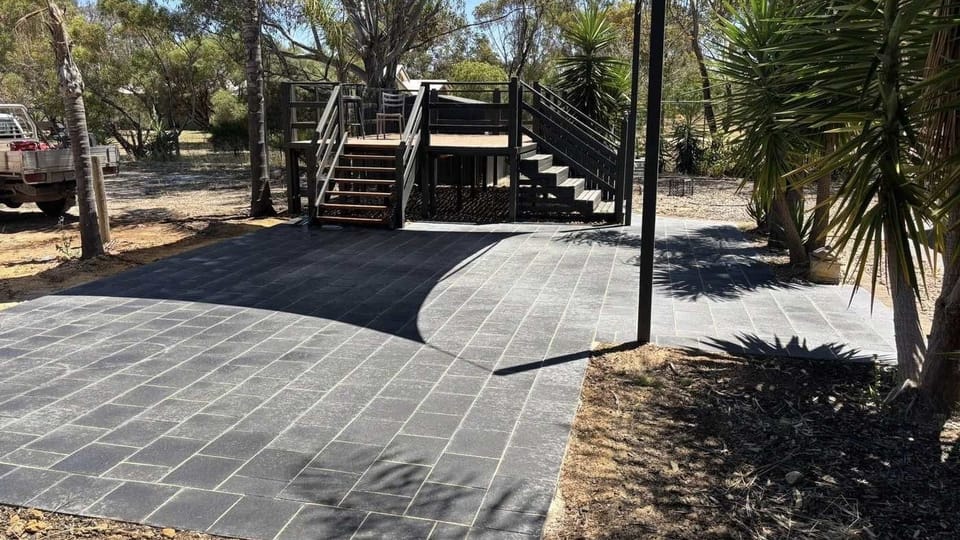 A wide charcoal paved patio leading to timber steps and a raised deck, laid by May Paving