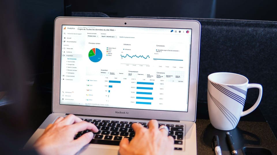 Hands typing on a laptop showing an analytics report, with a coffee mug beside it