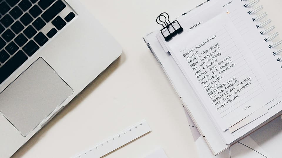 A laptop beside a handwritten checklist on a clipboard