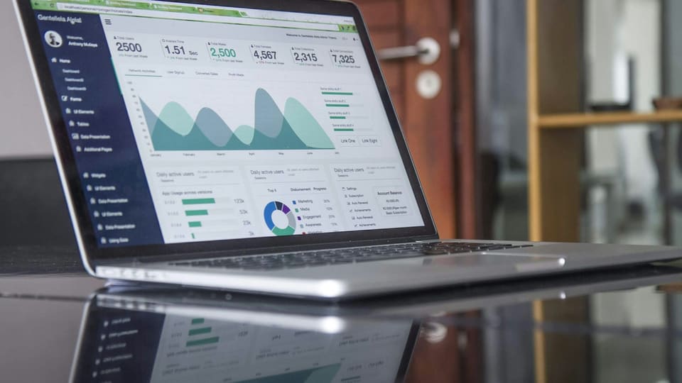 A laptop on a glass table showing a marketing dashboard full of charts